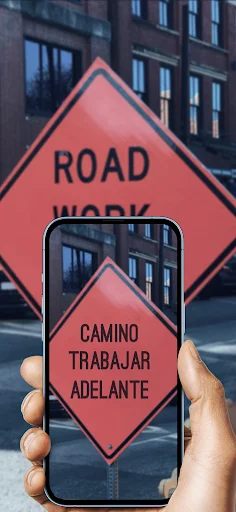 Hand holding smartphone translating English road work sign to Spanish text using photo translator image capture feature